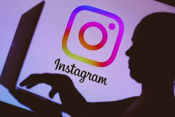 Silhouette of a person using a laptop with the Instagram logo displayed on the screen.