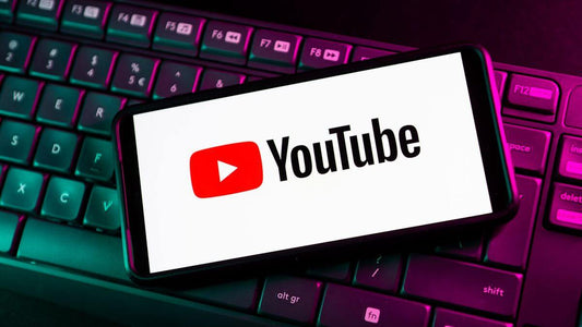 Smartphone displaying the YouTube logo on a keyboard in a colorful lighting setup.