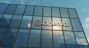 OpenAI logo displayed on a modern glass building with a clear blue sky in the background.