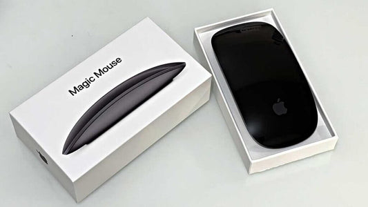 Magic Mouse in black color displayed beside its packaging box, showcasing sleek Apple design.